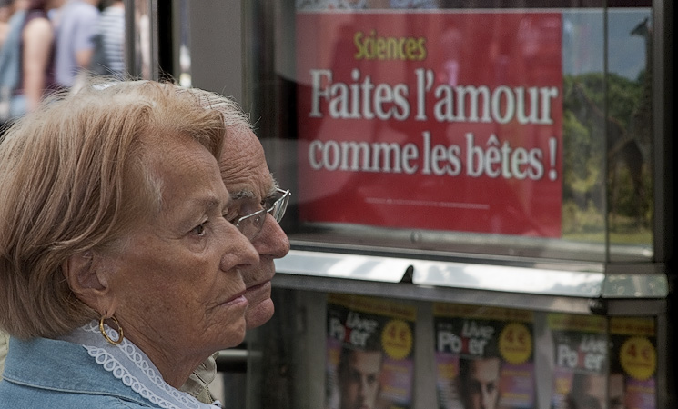 A couple in front of an advertisement for Marianne magazine with the headline «Faites l’amour comme les bêtes!», “Make love like animals”.
