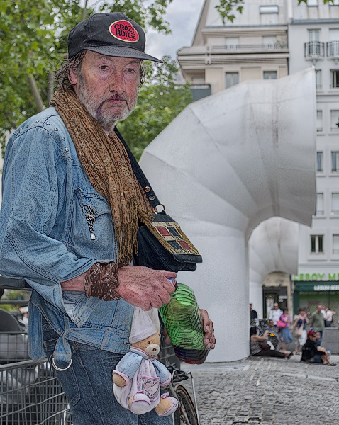 A homeless English man in front of the Pompidou Center with a bottle of cheap wine, a doodoo and a Crazy Horse baseball hat.
