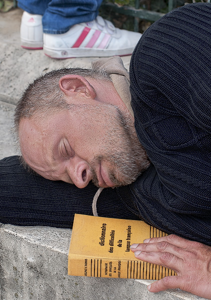 A homeless man sleeping on a book about the difficulties of the French language.