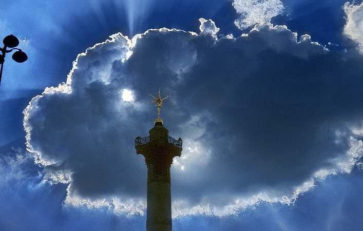 The sun shining through clouds behind the colonne de Juillet in place de la Bastille.