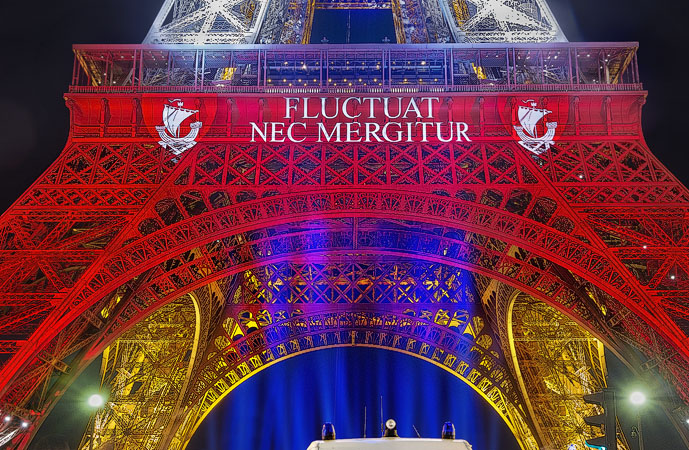 La tour Eiffel avec le slogan de la ville de Paris, Fluctuat nec mergitur projeté dessus la nuit.