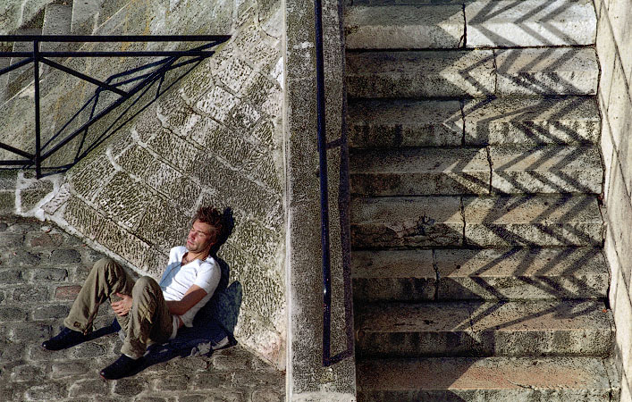 A man lying in the sun next to the stairs that lead down from quai de Bourbon under pont Saint-Louis.