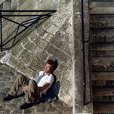 A man lying in the sun next to the stairs that lead down from quai de Bourbon under pont Saint-Louis.