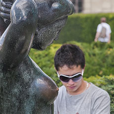 A sculpture and a young man looking at photos on the back of a digital camera in the Tuileries Gardens.