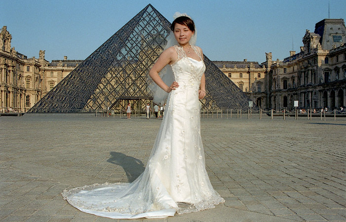 Une jeune mariée en tenu de mariage devant la Pyramide du musée du Louvre.