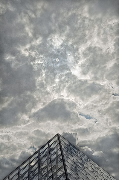 The sun shining through clouds behind the great pyramid in the cour Napoléon.