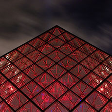 The Great Pyramid of the musée du Louvre lit up in red at night.