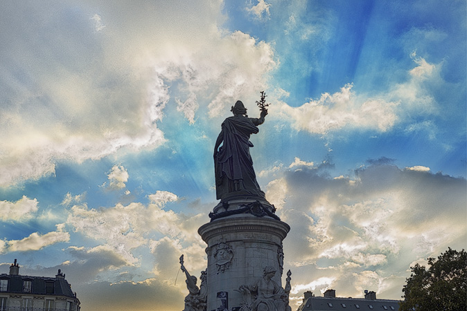 Le soleil brille à travers les nuages derrière la statue de Marianne dans la place la République.