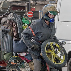 A packrat riding a heavily-loaded moped on quai du Louvre.