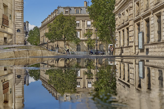 La caserne Napoléon et la place Baudoyer reflétées dans une flaque d’eau sur la rue François-Miron.