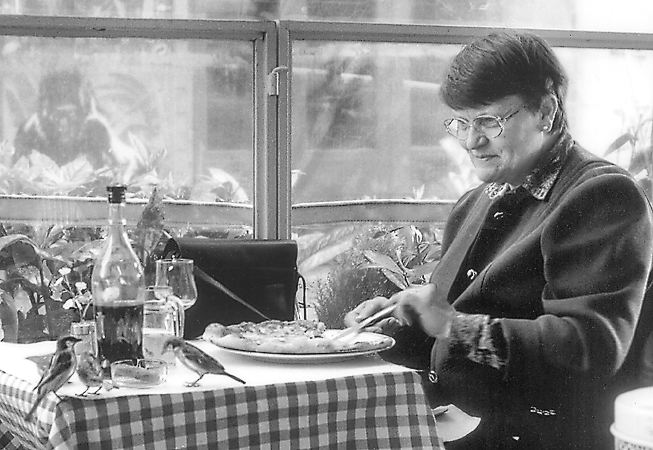 Une femme en train de déjeuner avec des moineaux dans la place Joachim-du-Bellay.