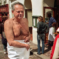 A man walking past place du Tertre wearing nothing but a bed sheet.