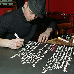 The barman writing up the specials of the day on the blackboard at «Le Sainte Marthe» in Paris.