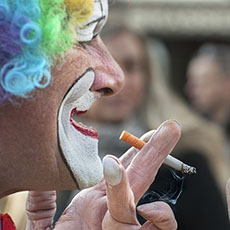 A clown looking at his makeup in a mirror while smoking in front of the Pompidou Center.