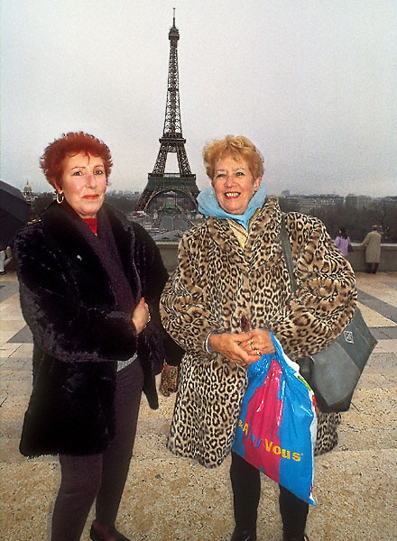 Two ladies, one wearing a leopard-skin coat, in front of the Eiffel Tower.