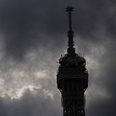 Le sommet de la tour Eiffel entouré des nuages gris.