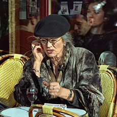 An older woman slamming her fist on a café table while talking on her cellphone on île Saint-Louis.
