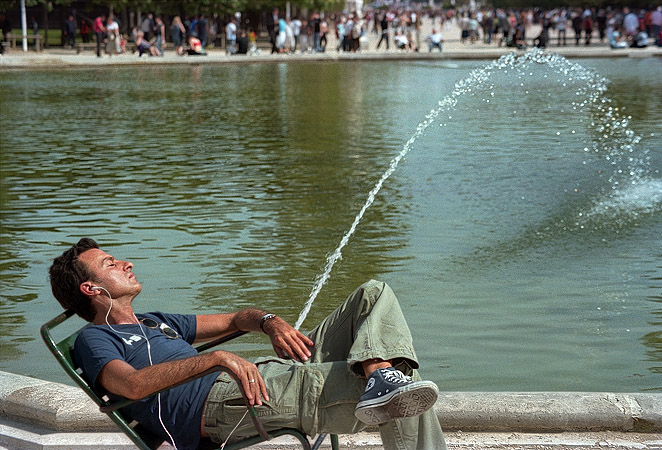 Un homme devant une fontaine du grand bassin rond dans le jardin des Tuileries en train d’écouter de la musique sur son iPod.