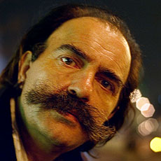Un homme sans domicile fixe avec une grande moustache dans la place de la Bastille le soir.