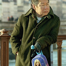 A middle-aged Asian man on pont au Double with a Barbie doll handbag.