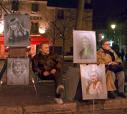 Un artiste avec quatre de ses tableaux dans la place du Tertre le soir.