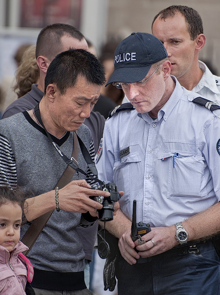A policeman looking at a tourist’s pictures in front of Notre-Dame.