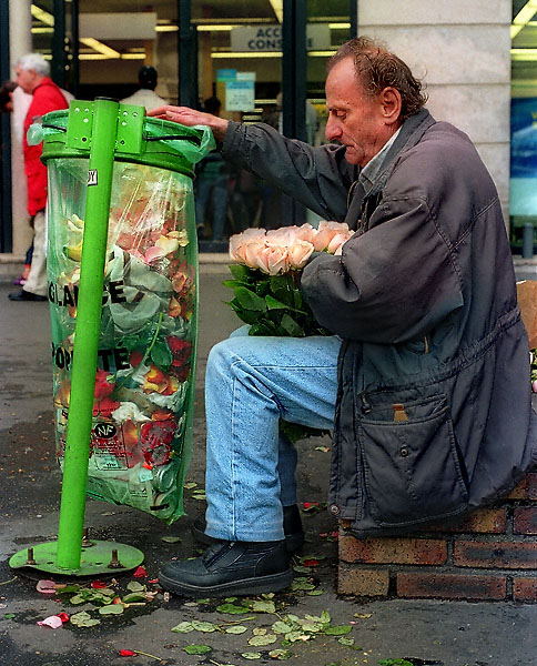 Un homme devant une poubelle dans la place de la République en train de préparer des roses pour les vendre.