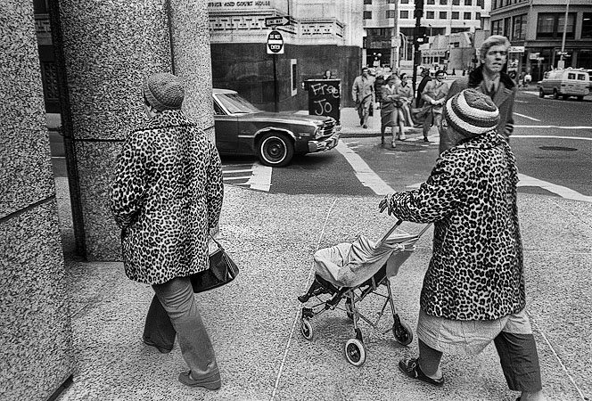 Two women dressed in leopard skin coats walking with a baby carriage near Post Office Square in Boston.