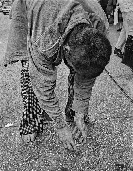 A homeless man playing with cigarette butts on the sidewalk in New York’s Times Square.