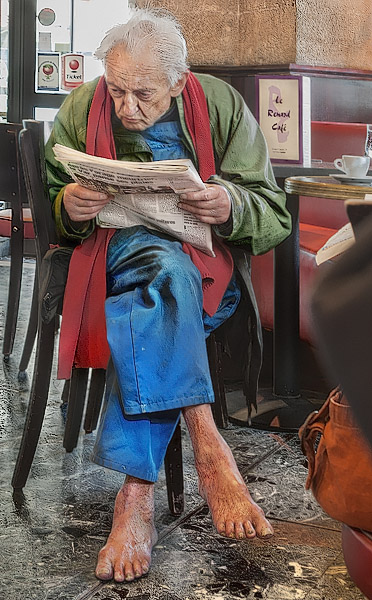 A barefoot homeless man reading a newspaper in a café.