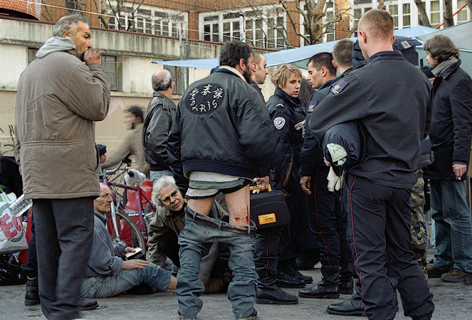 A homeless man whose leg is bleeding after being bitten by dogs, surrounded by policement and ambulance workers next to canal Saint-Martin.