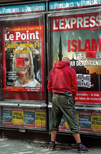 A (willfully) homeless man urinating on a newstand in front of a poster with the headline, «Islam, les vérités qui dérangent». (Disturbing truths about Islam).